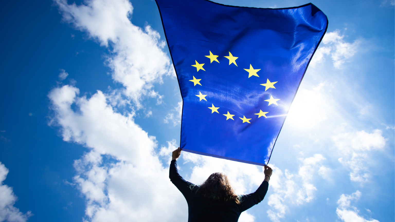 Eine Frau schwenkt eine EU-Fahne vor dem Himmel. – DJV Hessen-Landesvorsitzender Knud Zilian sowie der Vorsitzende des Fachausschusses Europa, Michael Schwab, rufen gemeinsam auf, vom Wahlrecht Gebrauch zu machen und zur Europawahl zu gehen.